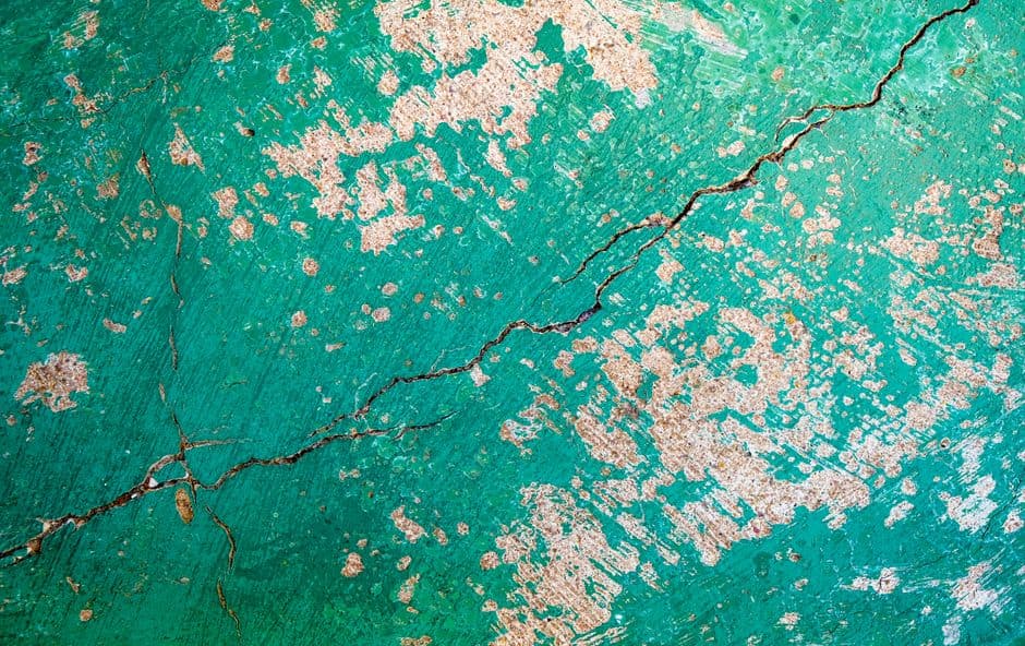 Close-up of a cracked, textured green wall with a peeling surface.